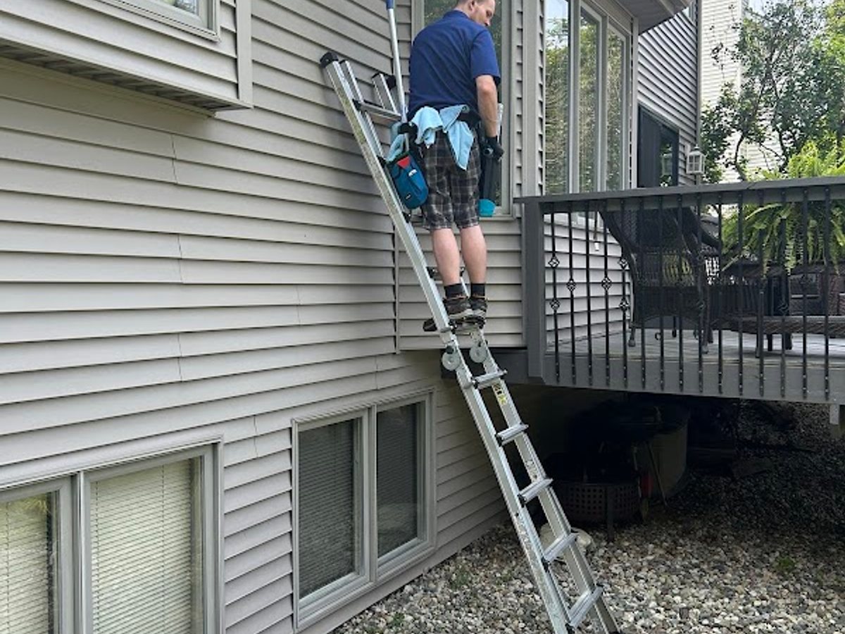A Godvision Cleaning technician on a ladder at the windows of a Battle Creek home