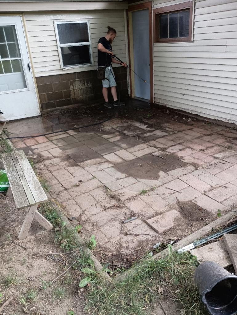 A Godvision crew member washing a house wall above a paver patio mid pressure-washing job