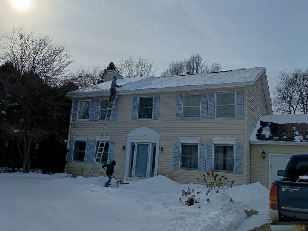 A snowy Battle Creek two-story home with a Godvision crew member clearing snow, truck in the drive